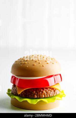 Creativo giocattolo di plastica hamburger con insalata, pomodoro e carne di manzo su sfondo grigio chiaro. Concetto di cibo artificiale nocivo. Non organico. Non utile. Foto Stock