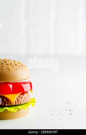 Creativo giocattolo di plastica hamburger con insalata, pomodoro e carne di manzo su sfondo grigio chiaro. Concetto di cibo artificiale nocivo. Non organico. Non utile. Foto Stock