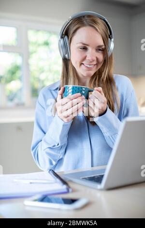 Donna che studiano a casa tramite laptop e indossa le cuffie Foto Stock