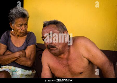 Uomo e donna seduti di fronte alla loro casa nel centro dell'era coloniale della città, Trinidad, Cuba Foto Stock