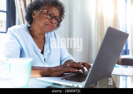 Donna afro-americana anziana che usa un computer portatile a casa durante il blocco della quarantena per coronavirus COV Foto Stock