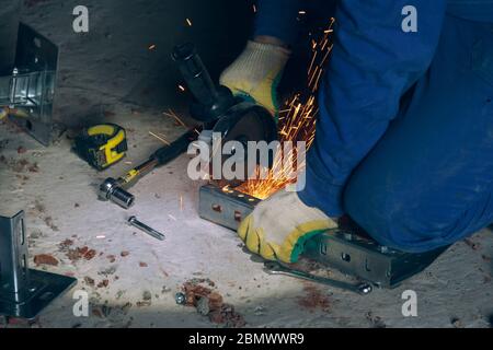 L'operatore taglia il metallo con una rettificatrice. Flusso di lavoro nel cantiere Foto Stock