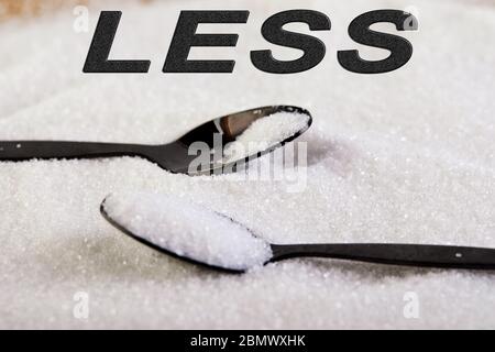 Meno testo zucchero. Lo zucchero scivola su un cucchiaio e mezzo cucchiaio, suggerendo un concetto di dieta e salute. Foto Stock