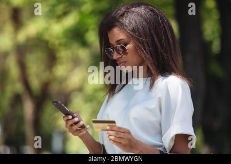 Donna in possesso di una carta di credito e utilizzando il telefono cellulare per gli acquisti online Foto Stock