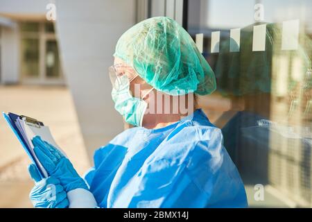 Gli infermieri di fronte alla clinica sono in attesa di visitatori con elenco per il monitoraggio dei contatti in coronavirus pandemico Foto Stock