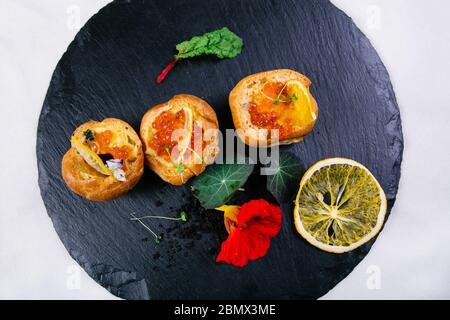 Panini con burro e caviale rosso, decorati con verdure, con fette di limone, una foglia di menta, un piatto con pezzi di burro accanto e un cucchiaio di wit Foto Stock