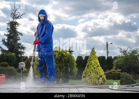 Manutenzione Caucasian Worker Power Lavaggio pavimentazione in cortile di casa. Foto Stock