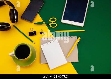 Cancelleria sulla vista del piano d'esame. Sfondo giallo e verde brillante. Blocco note per note con posto per testo. Lavoro a casa. Una tazza di caffè. Layout Foto Stock