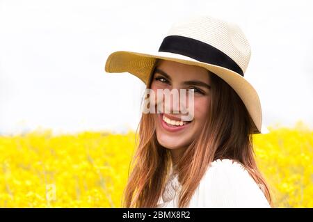 Primo piano ritratto esterno di giovane bella donna in piedi per un campo di fiori gialli Foto Stock