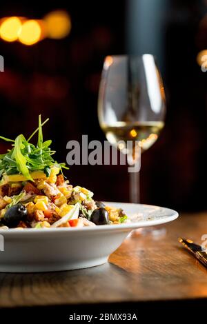 Insalata di Tun con olive, mais e rucola in tavola con un bicchiere di vino bianco Foto Stock