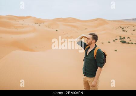 Uomo zaino in spalla viaggio in Marocco, deserto del Sahara. Guardando avanti ed esplorare la natura africana, dune di sabbia intorno. Foto Stock