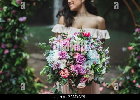 Sposa tenuta in mano incredibile bouquet fiorente enorme sulla cerimonia di nozze. Rosa rose, peonia, tulipani rossi e verdi primo piano. Foto Stock
