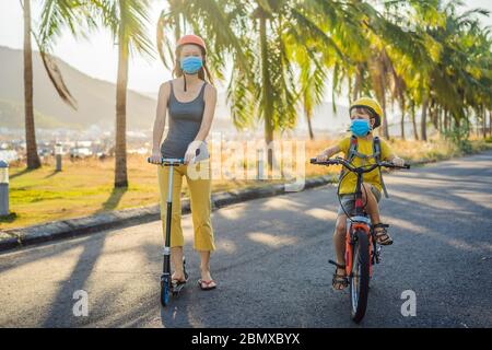 Bambino ragazzo scuola attiva e la sua mamma in maschera medica e casco di sicurezza in bicicletta con zaino in giornata di sole. Buon bambino in bicicletta sulla strada per la scuola. Tu Foto Stock