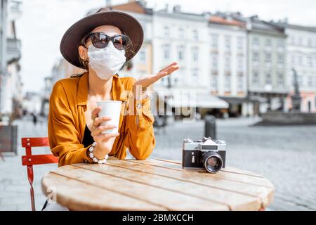 Donna disaccoppiata in maschera facciale seduta sulla terrazza del caffè da sola. Concetto di distanza sociale e nuove regole sociali dopo la pandemia di coronavirus. Foto Stock