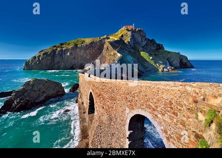 Ponte in pietra archiata che conduce ad una piccola isola rocciosa con piccola cappella sulla sommità Foto Stock