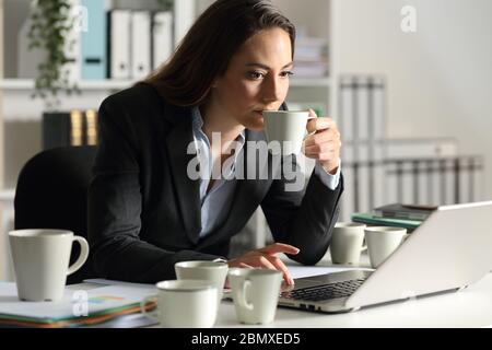 Donna executive che lavora troppo e ha bisogno di caffeina e ha diverse tazze di caffè seduti su una scrivania la notte in ufficio Foto Stock