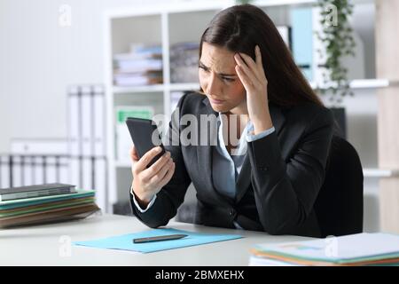 Triste executive donna leggere cattive notizie su smartphone seduto su una scrivania in ufficio Foto Stock