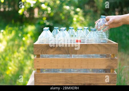 Riutilizzo del concetto di riciclaggio delle bottiglie in plastica. Mano dell'uomo lasciando una bottiglia di plastica in una scatola di legno riciclata con bottiglie di plastica senza un tappo con Foto Stock