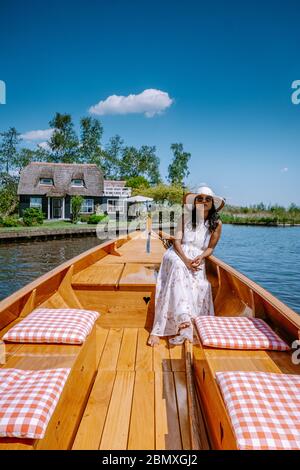 Giethoorn Olanda donna visitare il villaggio con una barca, vista del famoso villaggio con canali e case rustiche tetto di paglia in zona fattoria su un caldo Foto Stock