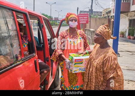 Una donna riceve un cartone di tagliatelle da un assistente privato durante la chiusura di Covid-19 a Lagos, Nigeria. Foto Stock