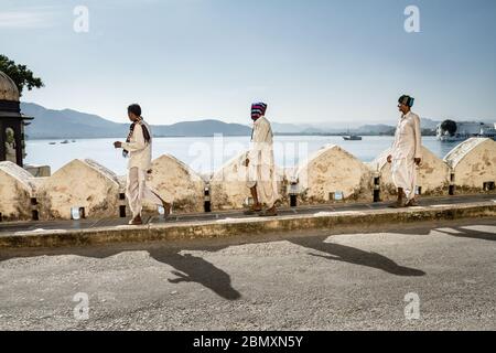 Udaipur, India - 19 Gennaio 2013. Tre uomini indiani vestiti in bianco camminano equidistanti l'uno all'altro prima del lago di Pichola, Palazzo di Udaipur Foto Stock