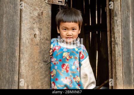 SOP Pong, Thailandia - 1 marzo 2013. Il ragazzino di una tribù di lisu si trova nei suoi pigiami all'ingresso di una piccola capanna di legno. SOP Pong, Thailandia Foto Stock