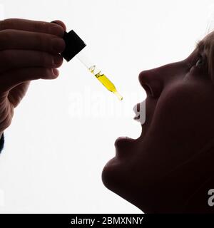 Silhouette di una donna che prende gocce di olio CDB Foto Stock