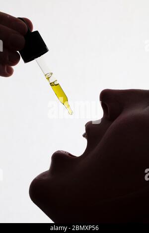 Silhouette di una donna che prende gocce di olio CDB Foto Stock