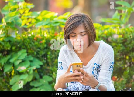 Donne asiatiche seduti sul marciapiede lungo la strada e giocare Mobile. Foto Stock