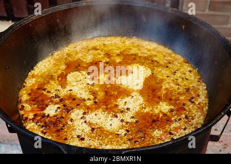 Piatto nazionale uzbeko pilaf, pilaw, plov, riso con carne in padella grande. Cottura processo, fuoco aperto. Cottura in un cavolone sul fuoco. Mescolare lentamente con un Foto Stock