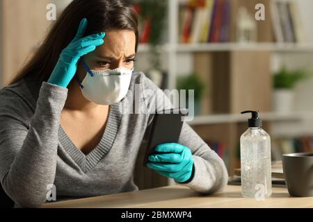 Donna preoccupata con maschera protettiva legge le notizie difettose del coronavirus sullo smartphone alla notte che siede a casa Foto Stock