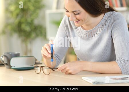 Donna felice serraggio viti fissaggio occhiali con cacciavite seduto su una scrivania a casa Foto Stock