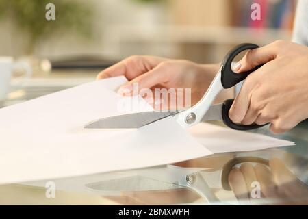 Primo piano delle mani della donna con forbici che tagliano carta su una scrivania a casa Foto Stock