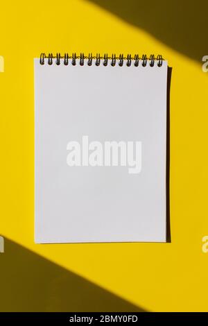 Pagina bianca vuota del notebook in una spirale su uno sfondo giallo luminoso con ombre. Vista dall'alto, spazio di copia. Foto Stock