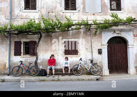 Madre e figlio seduti su una panchina davanti ad una casa tradizionale a Gorjansko - tipico villaggio di carst, slovenia Foto Stock