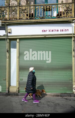 Vienna, Austria-Aprile, 20-2020: Donne anziane con maschera protettiva camminano un cane e passano un negozio vintage chiuso con il nome del negozio scritto in germe Foto Stock