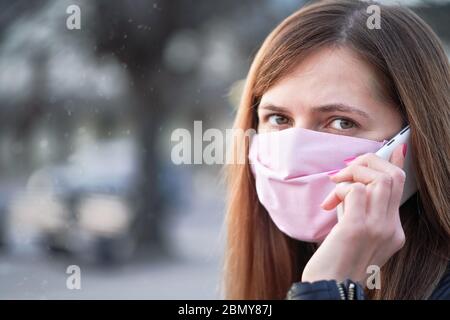 Giovane donna con rosa cotone fatto a mano faccia naso bocca maschera parlare sul suo telefono cellulare, ritratto chiuso. Può essere usato durante il co-19 out di coronavirus Foto Stock