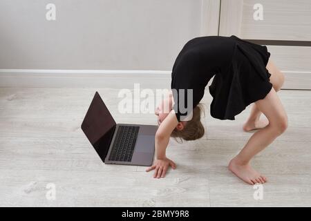 Studentessa guarda video online su un laptop e fa esercizi sportivi - yoga, ginnastica, coreografia. Rimani a casa. Concetto di autoisolamento Foto Stock