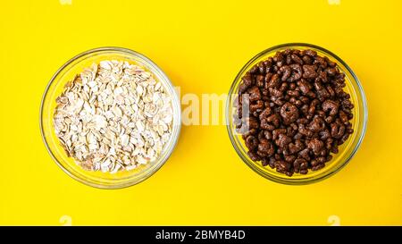 Due ciotole con colazione rapida di cornflakes di cioccolato e pasto di avena su baclground giallo brillante. Spazio di copia Foto Stock