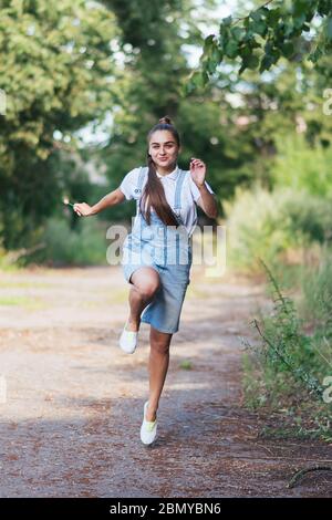 Una ragazza in tuta denim sorride e corre all'aperto. Foto Stock