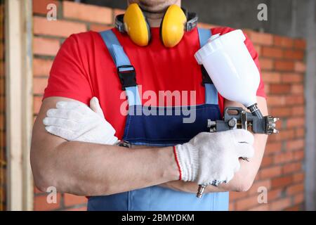 Primo piano costruttore che tiene la pistola a spruzzo nelle sue mani Foto Stock