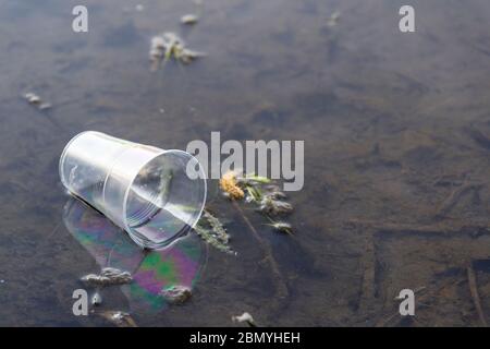 Una tazza di plastica usa e getta è stata gettata nel fiume. Inquinamento della natura. Inquinamento idrico. Tutela dell'ambiente. L'idea dei pericoli della plastica Foto Stock