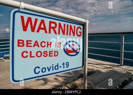 La spiaggia è chiusa a causa del cartello di avvertimento Covid-19 all'ingresso della spiaggia. Campagna sui social media per la prevenzione del coronavirus. La vacanza è annullata Foto Stock
