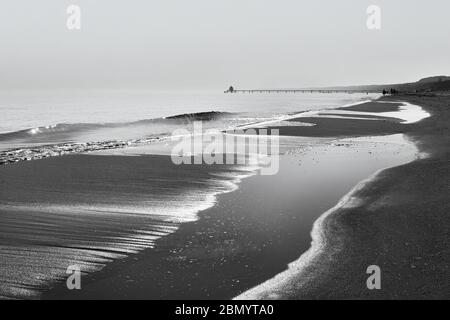 Vista lungo la linea d'acqua con onde, superfici d'acqua e camminatori, nonché un molo sullo sfondo - immagine in bianco e nero - posizione: Mar Baltico Foto Stock