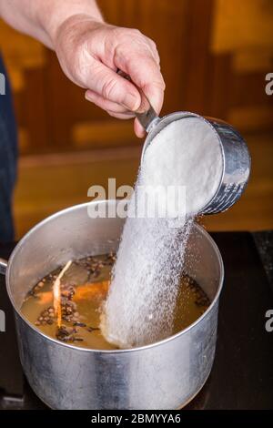 Donna che versa lo zucchero nella soluzione di decapaggio dell'aceto di sidro di mele, cannella cruda, spezie intere e chiodi di garofano interi utilizzati per inscatolare le barbabietole sottaceto. Foto Stock