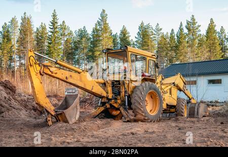 Primo piano vista posteriore sul vecchio escavatore giallo che si trova accanto al garage per scavi forestali, preparando il posto per la nuova costruzione. Svezia settentrionale, Umea. Foto Stock