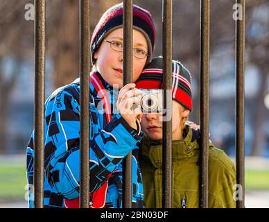 Fratelli che fotografano attraverso le barre di recinzione a Parigi, Francia Foto Stock