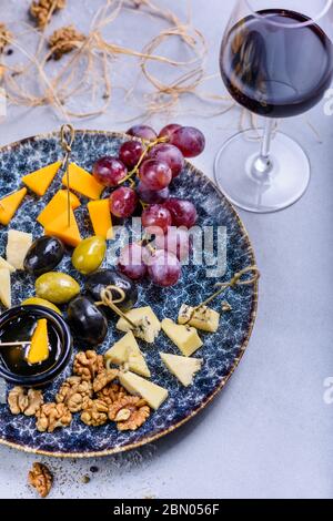 Piatto di formaggio con uva e olive. Spuntini e formaggi serviti con vino rosso. Vista superiore, spazio di copia. Foto Stock