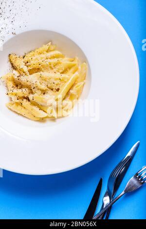 Gustosa e appetitosa pasta di penne classiche italiane con salsa cremosa e parmigiano al piatto su tavola blu. Vista dall'alto. Foto Stock