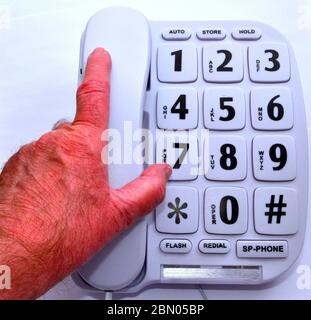 La mano di un uomo anziano o anziano prende il microtelefono di un telefono fisso grande tasto che è rivolto agli utenti anziani, disabili e ipovedenti Foto Stock